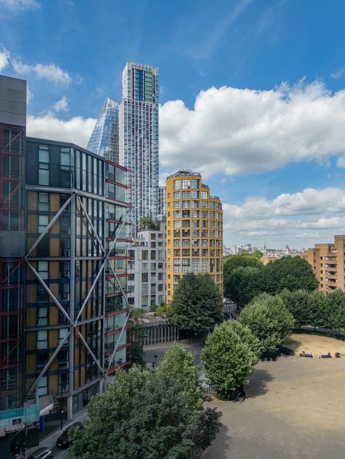 A tall modern skyscraper with a glass facade and a construction scaffolding structure on its side is visible on the left, set against a bright blue sky with scattered white clouds. In the middle dista